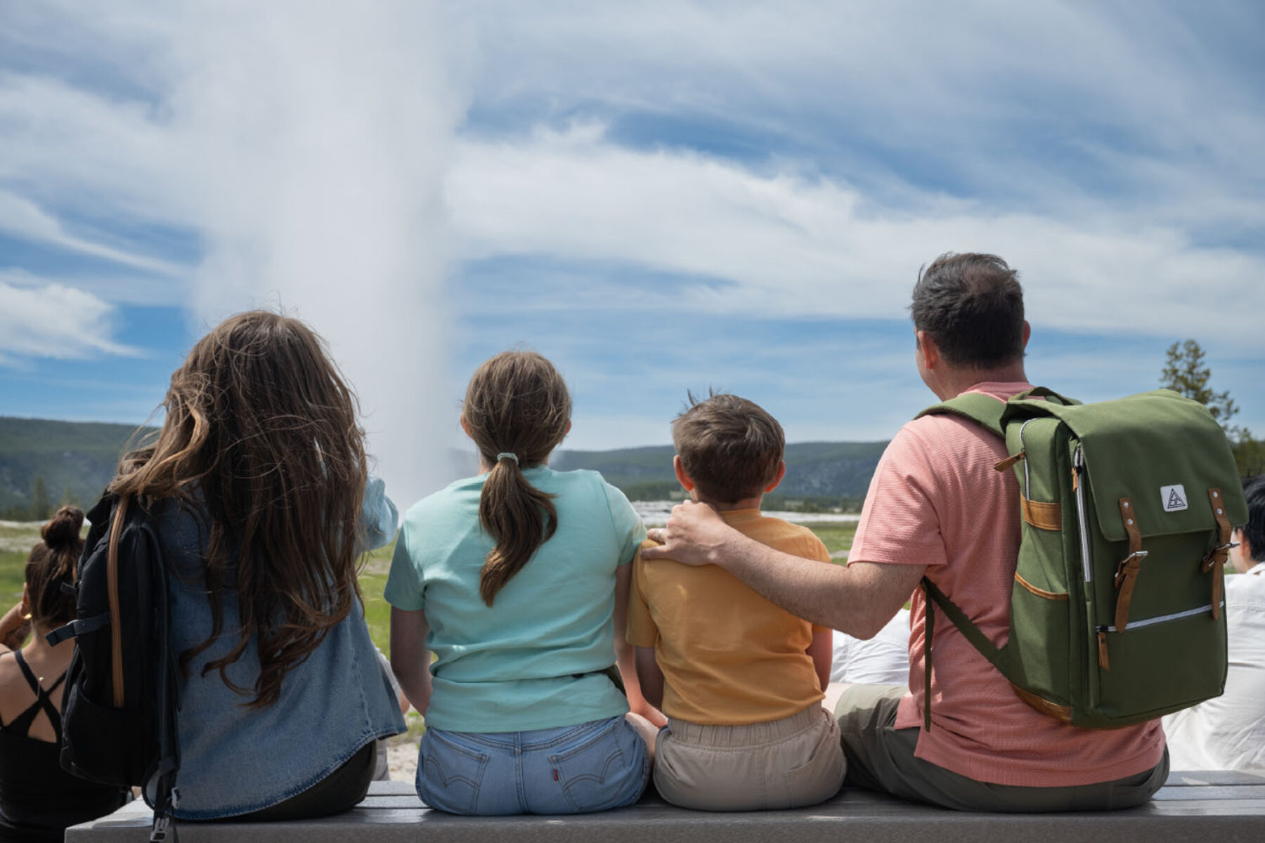A family sits on a bench, watching a geyser in Yellowstone National Park