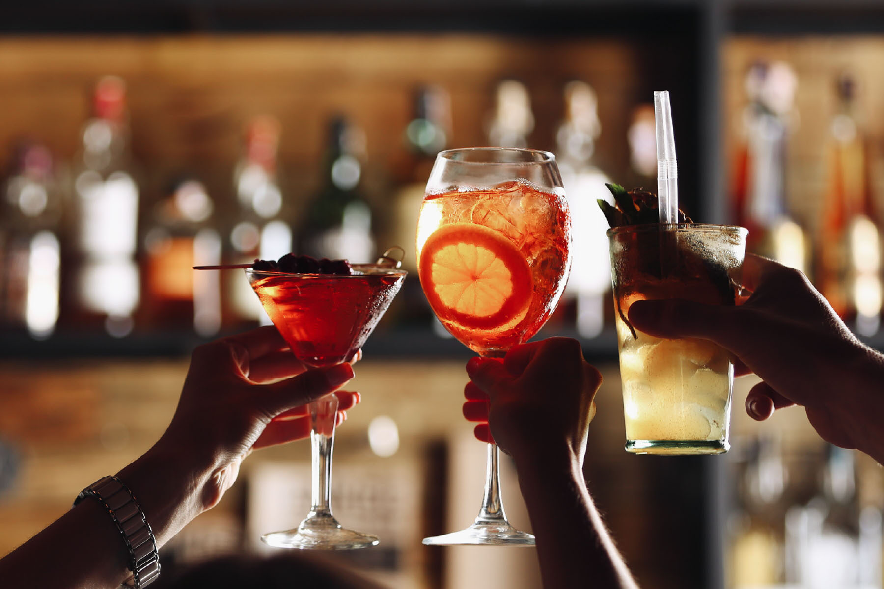 Three hands holding up their cocktails.