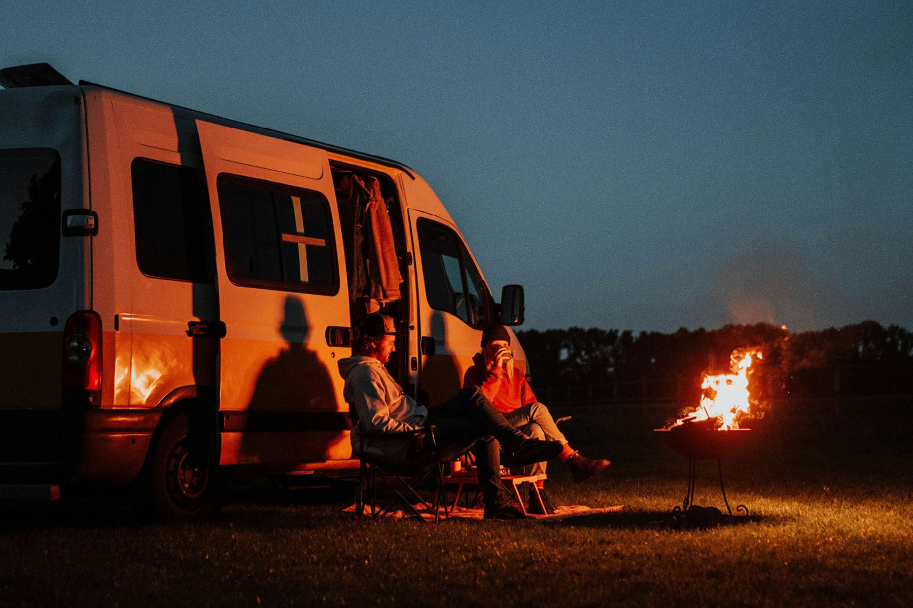 A couple sits by a fire outside their camper van