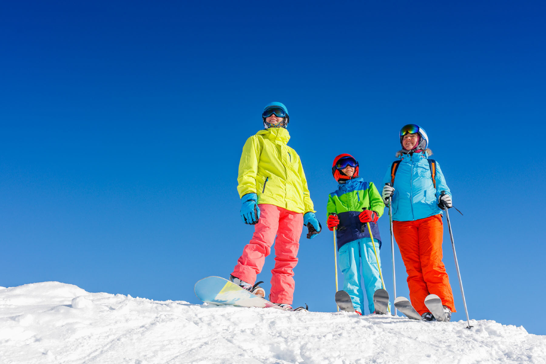 Two adults and a child in ski and snowboard gear with a blue sky background